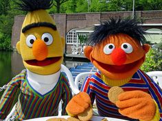 two sesame street characters sitting at a table with food and drink in front of them