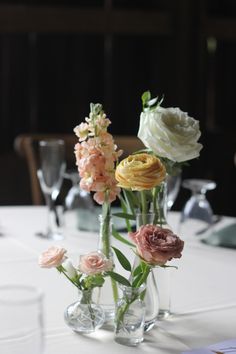 flowers in vases on a table with wine glasses and napkins around it,