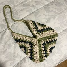 a crocheted purse sitting on top of a white bed next to a wooden floor