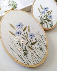 two embroidery hoops with flowers on them sitting next to an open book and some books