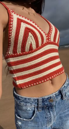 a woman standing on top of a sandy beach wearing a red and white striped crop top