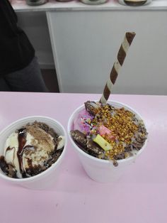 two bowls filled with ice cream and toppings on top of a pink countertop