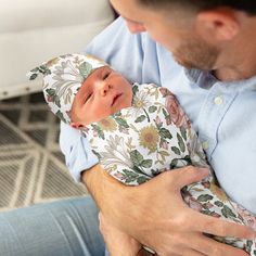 a man holding a baby in his arms and wearing a flowered wrap on it's head