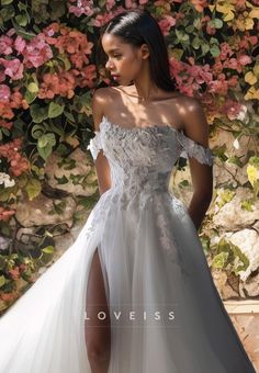 a woman in a white wedding dress standing next to a wall with flowers on it