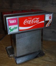 an old fashioned coca - cola machine sitting on top of a wooden table