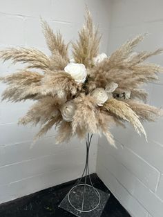 an arrangement of dried flowers in a vase on a black stand against a white brick wall