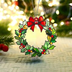 a stained glass christmas wreath ornament hanging from a tree with lights in the background