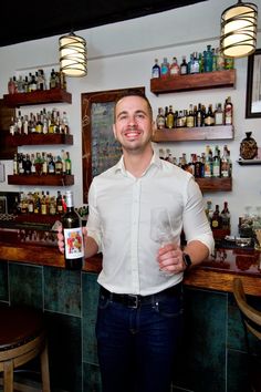 a man standing in front of a bar holding a wine glass and smiling at the camera