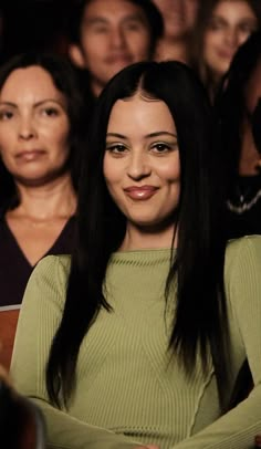 a woman with long black hair sitting in front of a group of people, smiling at the camera