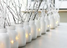 there are many white jars with branches in them and some lights on the top one