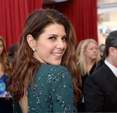 a woman in a green dress smiling at the camera with other people standing around her