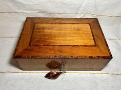 an open wooden box with a tassel on the side sitting on a white cloth