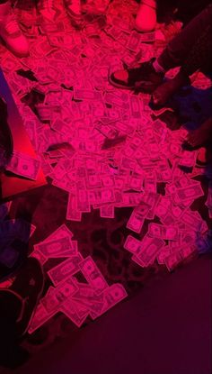 a pile of money sitting on top of a floor next to a red neon light