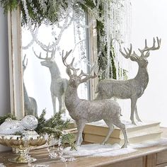 two silver deer statues sitting on top of a wooden table next to a mirror and christmas decorations