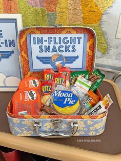 an old suitcase filled with snacks on top of a wooden table next to a map