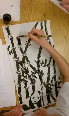 two people working on some art work at a table with papers and inkbrushes