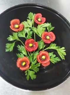 some red flowers and green leaves on a black plate