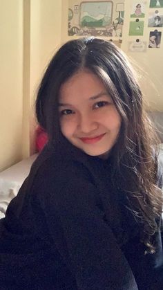 a young woman sitting on top of a bed next to a white wall in a bedroom