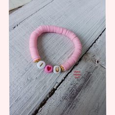 a pink beaded bracelet with white and gold beads on top of a wooden table