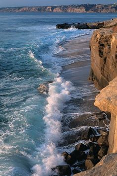 waves crashing on the beach and rocks near the water's edge, with cliffs in the background