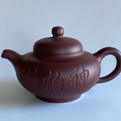 a brown teapot sitting on top of a white table next to a cup with writing on it