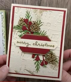 someone is holding up a christmas card with pine cones and evergreens on it, which reads merry christmas