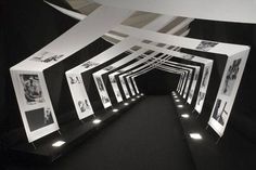 a black and white photo tunnel with pictures hanging on the wall, lit up by lights