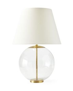 a clear glass lamp with a white shade on it's side and a gold base