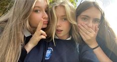 three young women standing next to each other with their hands on their mouths and looking at the camera