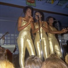 three women in gold outfits singing on stage