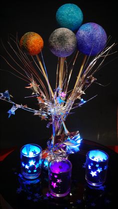 a glass vase filled with candles and some balls on top of a black tablecloth