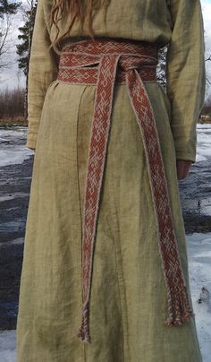 a woman wearing a long dress with a red sash around her waist, standing in the snow