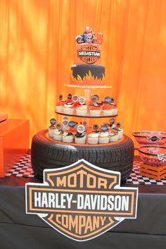 a motorcycle themed birthday cake and cupcakes on a table with an orange backdrop