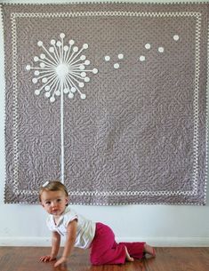 a baby crawling on the floor in front of a wall hanging with a flower design