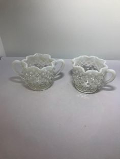 two white glass cups sitting on top of a table next to an empty cup and saucer