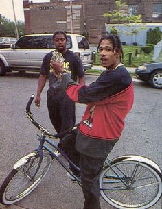 two men standing next to each other on the street with their bikes in front of them