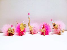 three gold and pink figurines are lined up against a white wall, one is wearing a tiara