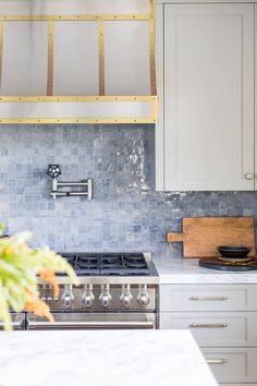 a kitchen with white cabinets and marble counter tops, gold trimming on the hood