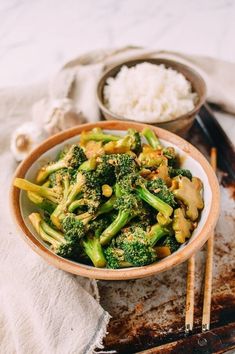 a bowl filled with broccoli and white rice next to chopsticks on a table