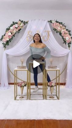 a woman sitting on top of a stool in front of a white backdrop with flowers