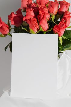 a bouquet of red roses in a white vase with a blank card on the side