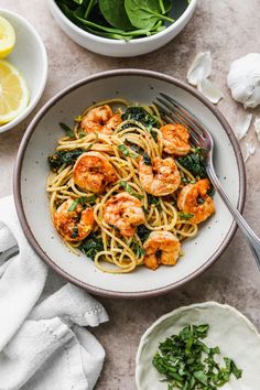 pasta with shrimp and spinach in a white bowl next to lemons, parsley and garlic