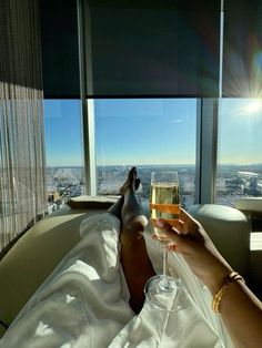 a person laying down with a glass of wine in their hand and looking out the window