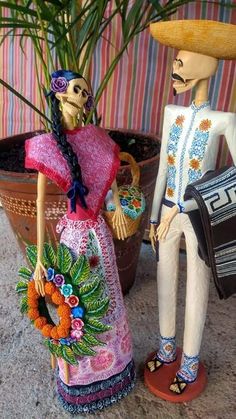 two figurines are standing next to each other in front of a potted plant