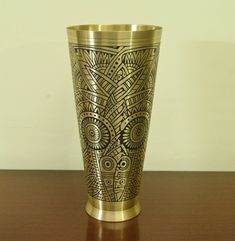 a gold colored metal vase sitting on top of a wooden table next to a white wall