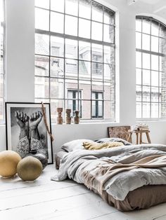 an unmade bed sitting in front of two large windows with pictures on the wall