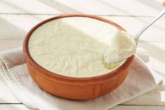 a wooden bowl filled with cream sitting on top of a white cloth next to a spoon