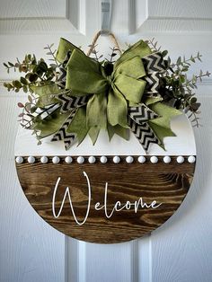 a welcome sign hanging on a door with green leaves and greenery attached to it