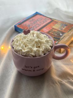 a pink cup filled with whipped cream next to a book