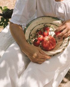 a woman holding a plate with tomatoes on it in her hands while sitting down outside